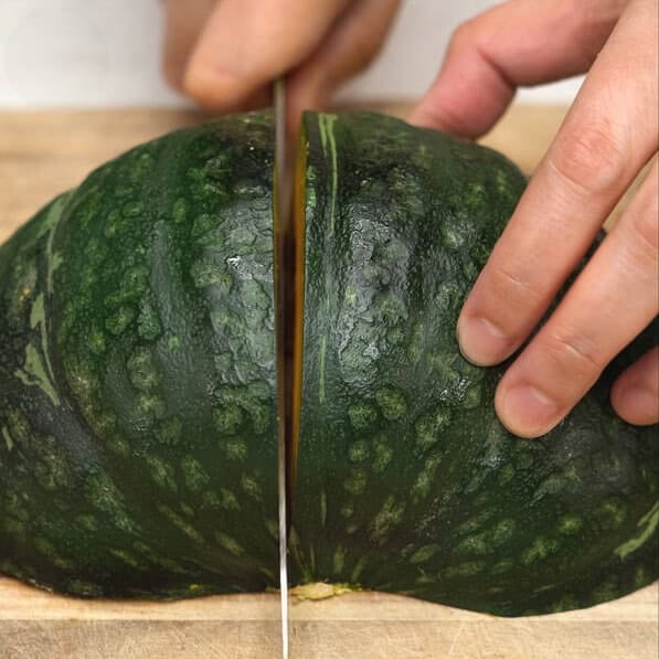 Cutting kabocha squash into quarters, then slicing off the stem.