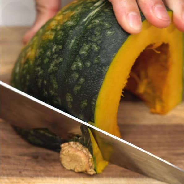 Cutting kabocha squash into quarters, then slicing off the stem.