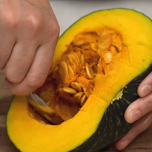 Cutting kabocha squash in half, then scooping the seeds with a spoon.