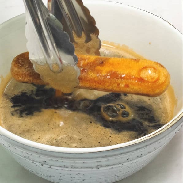 Dipping the ladyfinger in the coffee syrup using a small pair of tongs. Spreading mascarpone mixture on top of the layer of ladyfingers in the baking dish.