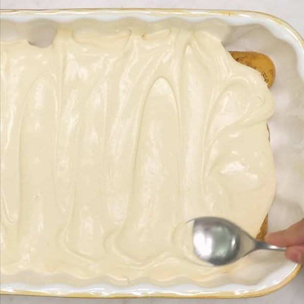 Dipping the ladyfinger in the coffee syrup using a small pair of tongs. Spreading mascarpone mixture on top of the layer of ladyfingers in the baking dish.