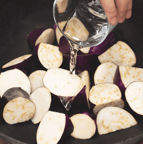 Adding water to steam the eggplant in the wok.