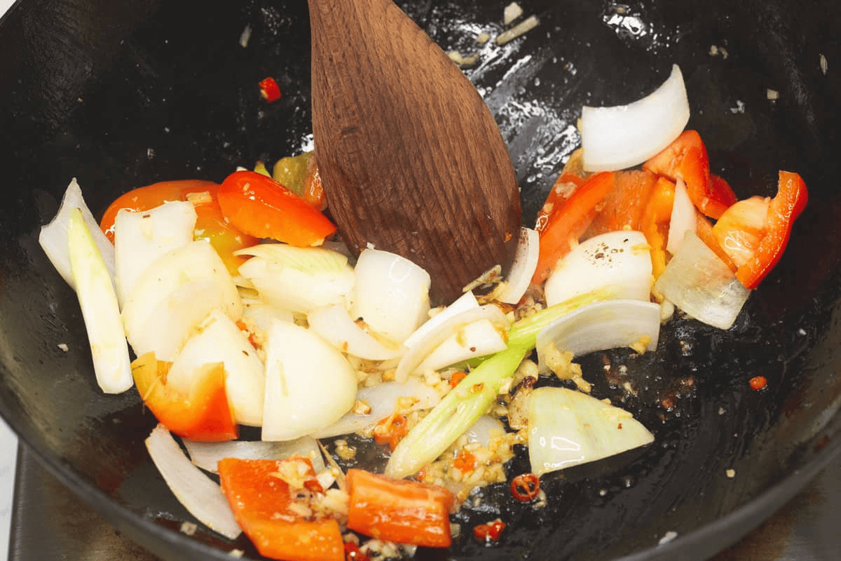Stir-frying the peppers and onions with the aromatics in the wok.