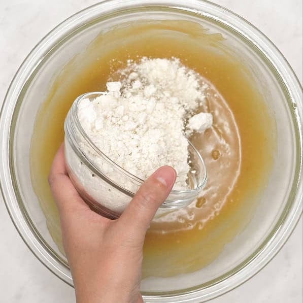Adding flour to the wet ingredients in the bowl. Folding the flour into the batter.