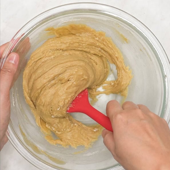 Adding flour to the wet ingredients in the bowl. Folding the flour into the batter.