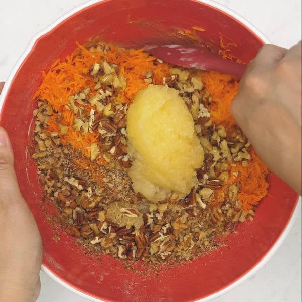 Added nuts, pineapple, and carrots to the mixture in the bowl. Mixing the cake batter using a spatula.