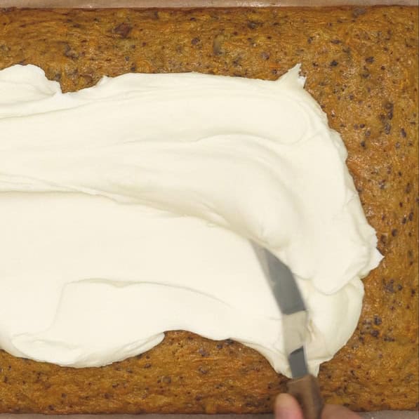 Spreading the cream cheese frosting onto the cake. Carrot sheet cake with cream cheese frosting topped with nuts.