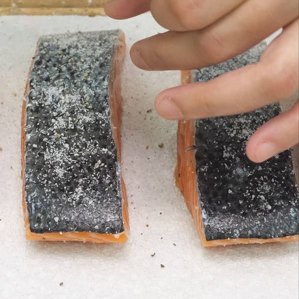 Seasoning the salmon fillets. Pan-frying the fillets while pressing against the pan.