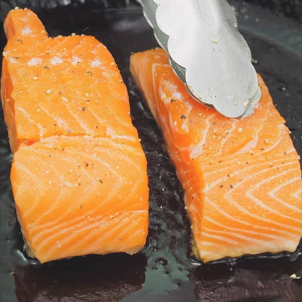 Seasoning the salmon fillets. Pan-frying the fillets while pressing against the pan.