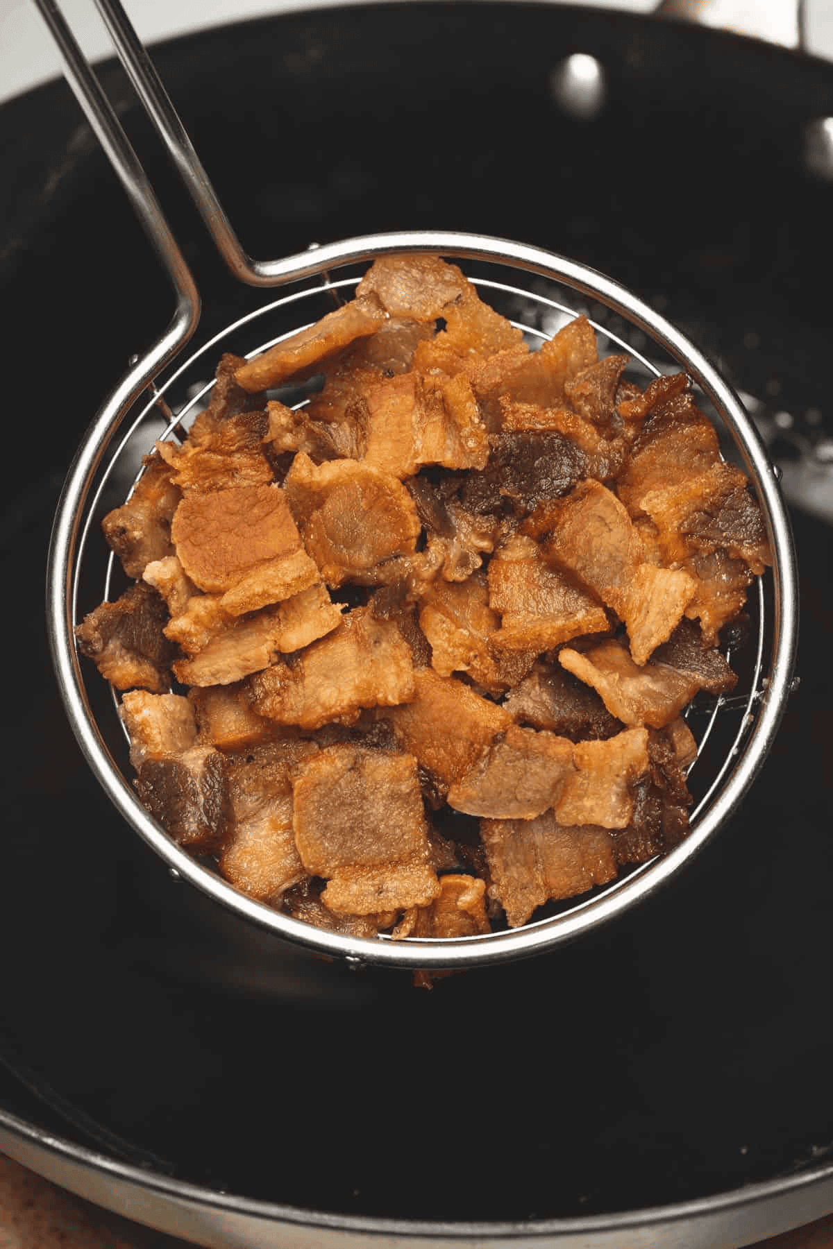 Fried pork belly slices in a skimmer.