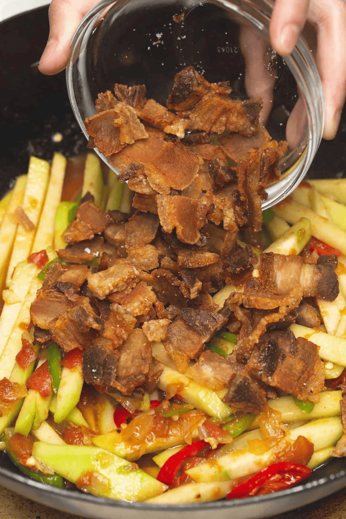 Adding fried pork to the chayote and ohter ingreadients in the wok.