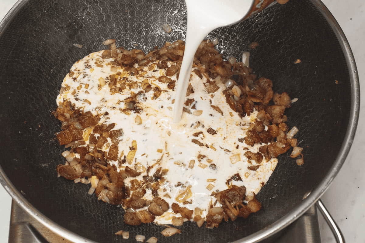 Adding the coconut milk to the aromatics and pork in the wok.