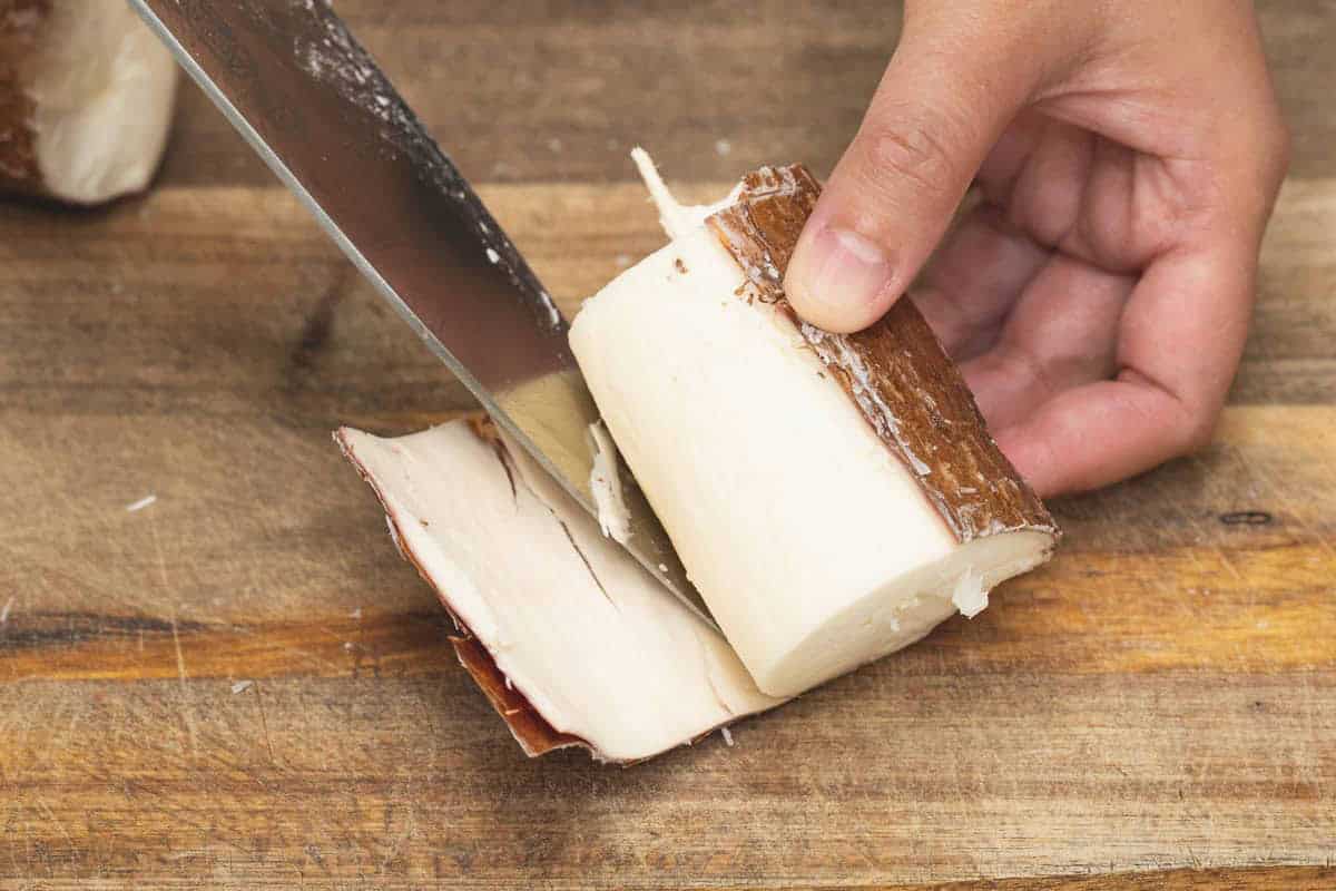 Lifting off the thick skin of the cassava using a knife.