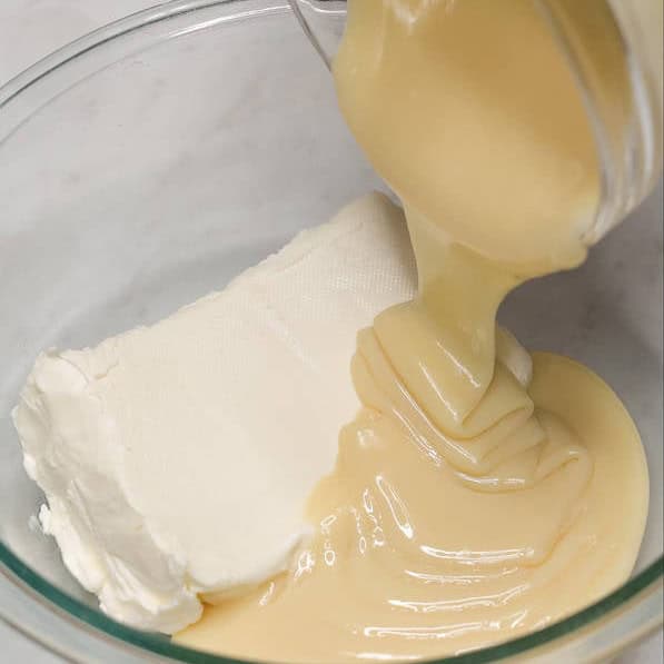 Adding condensed milk to the cream cheese in a bowl. Mixing the cream sauce with a whisk.