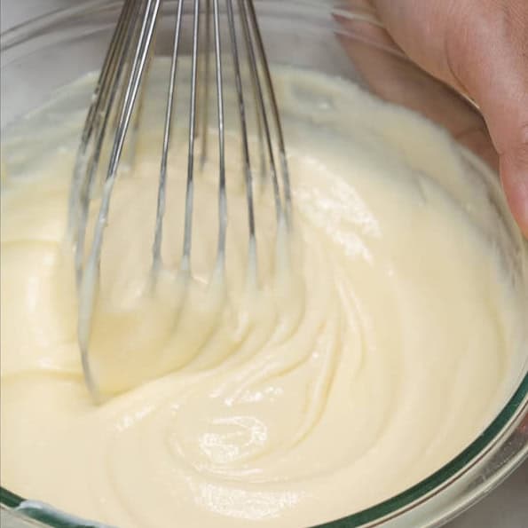 Adding condensed milk to the cream cheese in a bowl. Mixing the cream sauce with a whisk.