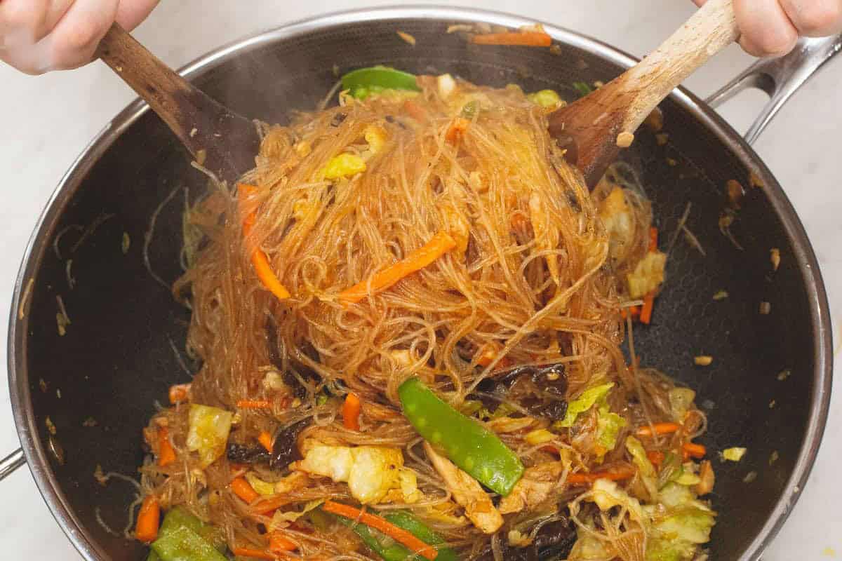 Tossing the Sotanghon Guisado in the wok using two wooden spoons.