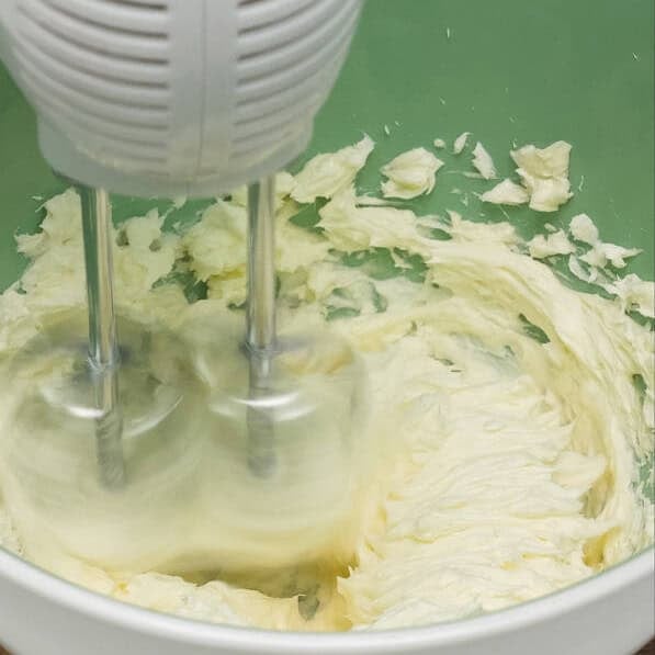 Mixing the cream cheese mixture using a hand mixer. Adding powdered sugar to the cream cheese mixture.