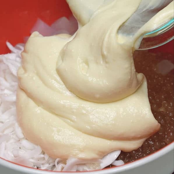 Adding the cream sauce to the bowl coconut strips, nata de coco, and sago. Mixing the salad mixture in the bowl.