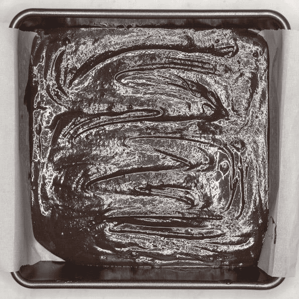 Brownie batter spread in a parchment-lined baking pan.