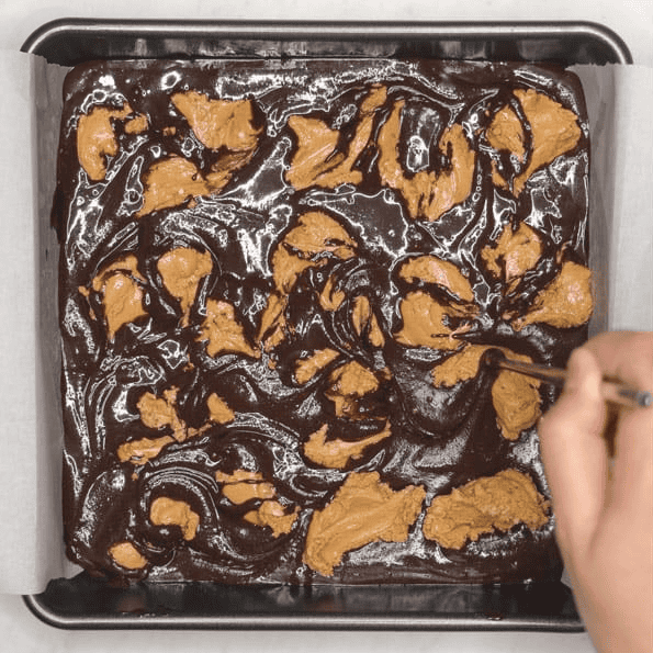 Swirling peanut butter mixture into brownie batter with a chopstick.