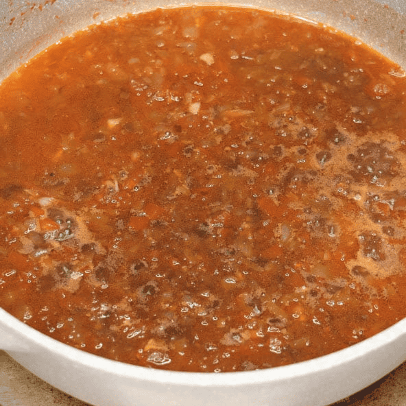 Simmering the tomato and shrimp paste broth for pinakbet.