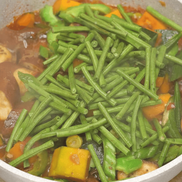 Adding yardlong beans to the vegetables.