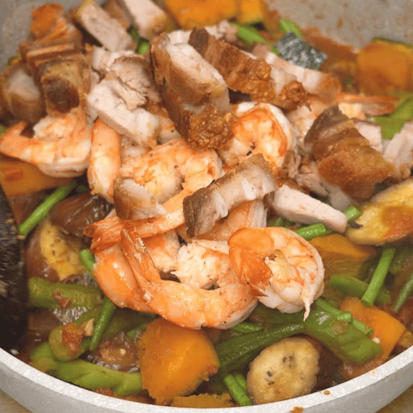 Adding seared shrimp and crispy pork belly to pinakbet.