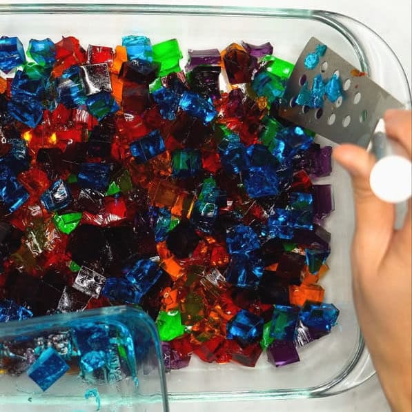 Arranging the multicolored jello cubes in the dish. Pouring the creamy gelatin mixture over the jello cubes.