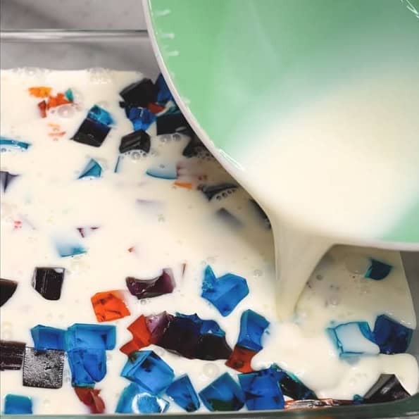 Arranging the multicolored jello cubes in the dish. Pouring the creamy gelatin mixture over the jello cubes.