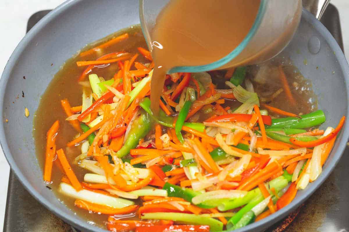 Pouring the sauce to the aromatics and vegetables in the skillet.