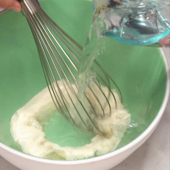 Whisking the gelatin powder while water is being poured into the bowl. Adding the condensed milk into the creamy gelatin mixture.