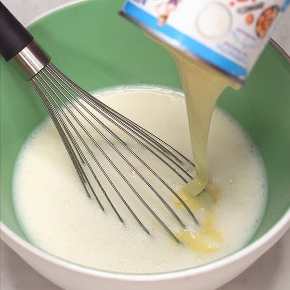 Whisking the gelatin powder while water is being poured into the bowl. Adding the condensed milk into the creamy gelatin mixture.