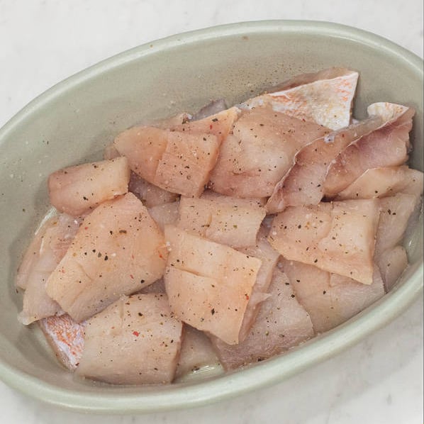 Fish fillets cut into smaller pieces, scored, and seasoned. Coating a piece with starch.