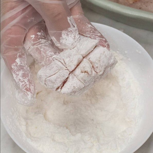 Fish fillets cut into smaller pieces, scored, and seasoned. Coating a piece with starch.