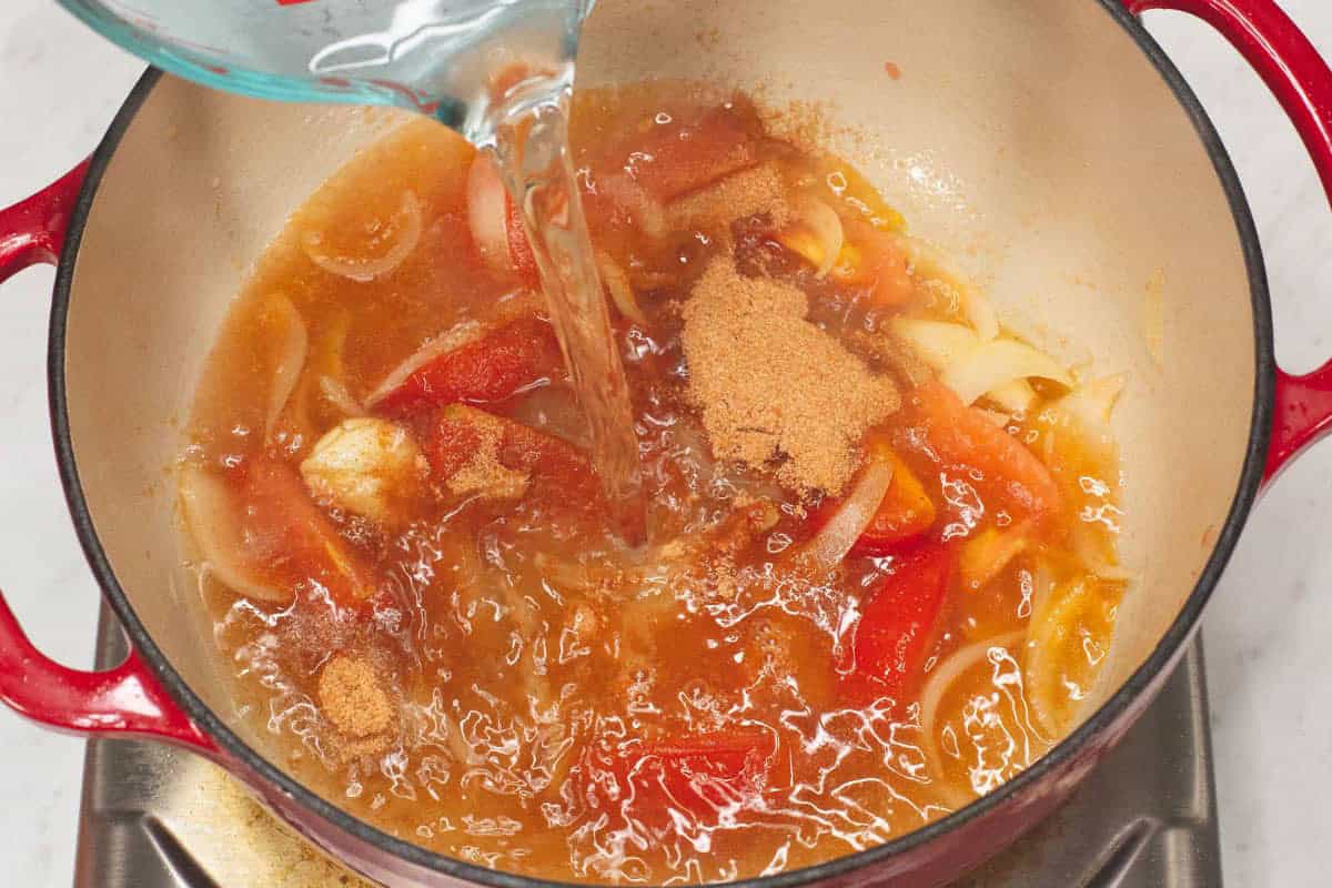 Adding water to the aromatics and sinigang mix in the pot.