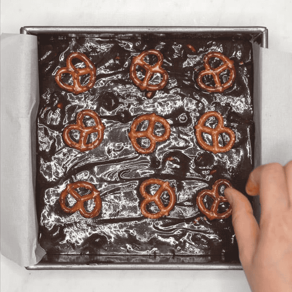 Arranging pretzels on brownie batter in a square baking pan.