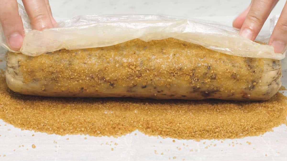 Rolling the log-shaped dough in turbinado sugar.