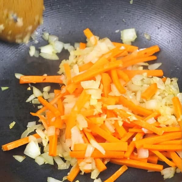 Sauteing onion, garlic, and carrots in a wok. Pouring the sauce to the aromatics and carrots in the wok.