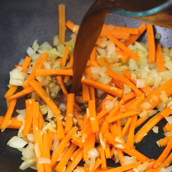 Sauteing onion, garlic, and carrots in a wok. Pouring the sauce to the aromatics and carrots in the wok.