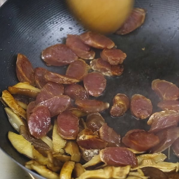 Browning Chinese sausages with shitake mushrooms in a wok. Shitake mushrooms, Chinese sausage, and shrimp in a wok.