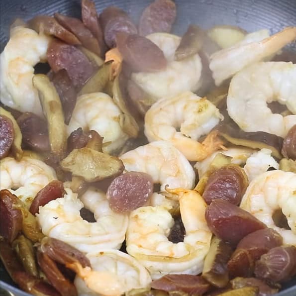 Browning Chinese sausages with shitake mushrooms in a wok. Shitake mushrooms, Chinese sausage, and shrimp in a wok.