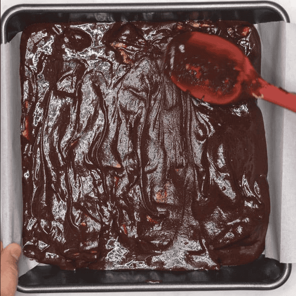 Spreading brownie batter in a square baking pan.