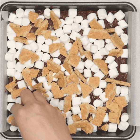 Adding marshmallows and graham crackers to baked brownies.
