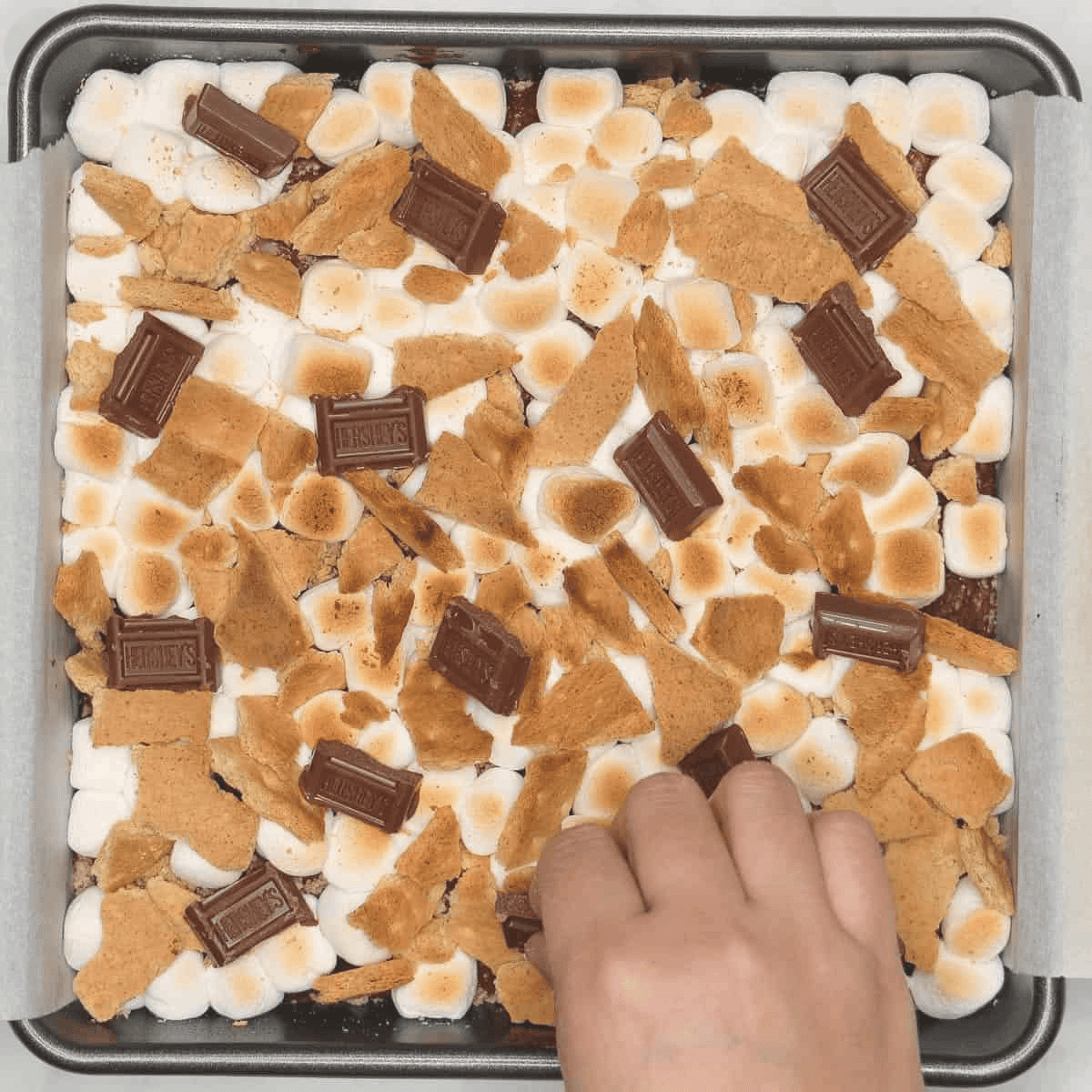 Adding chocolate pieces to toasted marshmallows and graham crackers on brownies.