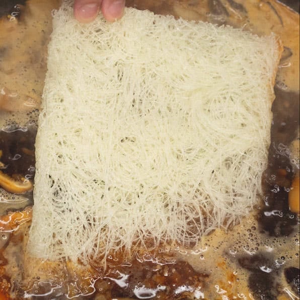 Soaking the dried noodles in the boiling stock until tender.