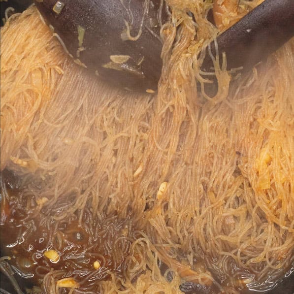 Soaking the dried noodles in the boiling stock until tender.