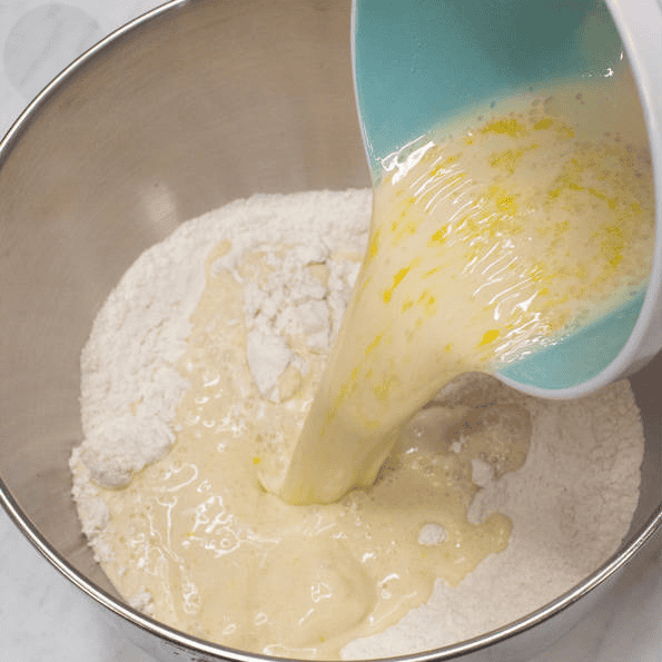 Pouring wet ingredients into flour in a mixing bowl.
