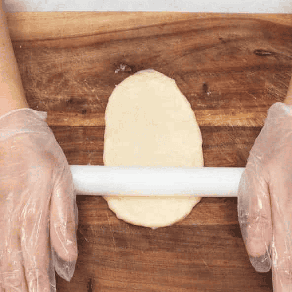 Rolling a portion of dough into an oval.