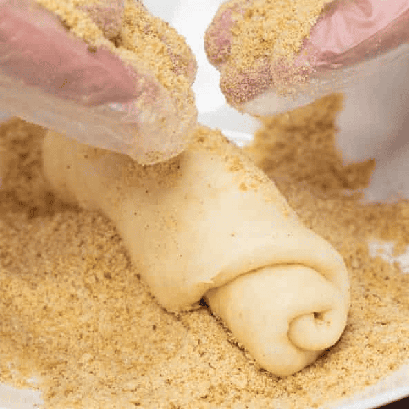 Coating the Spanish bread roll with breadcrumbs.