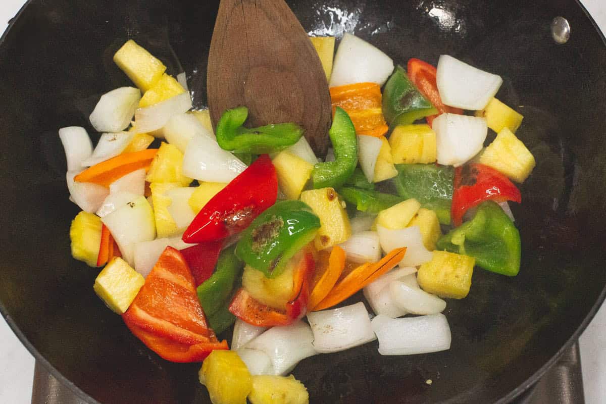 Stir-frying the vegetables and pineapple in a wok.